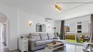 A modern living room with a grey sofa, a small white side table, and a wooden coffee table. There is a large window with a view of a building and a balcony. - Erisa 1-29. Terrace, Swimming Pool, Second line of beach (Torremolinos)