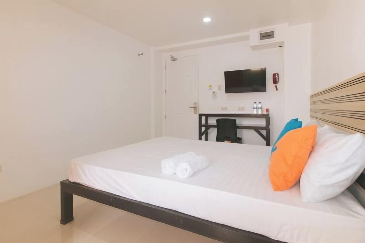 Une chambre d’hôtel avec un lit, un bureau, une chaise, une télévision et une porte.