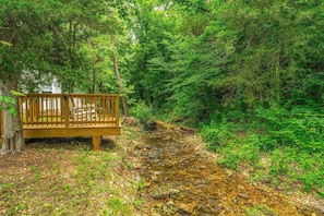 A wooden bench by a forested area with a stream.