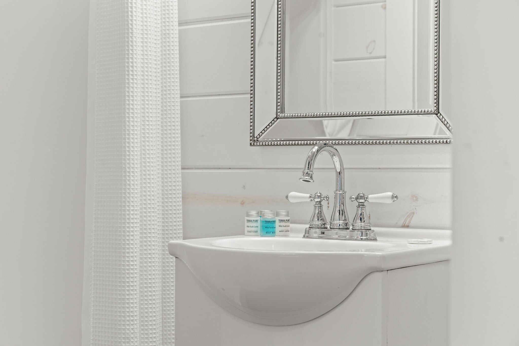 A white bathroom with a sink, a mirror, and two jars of toiletries.