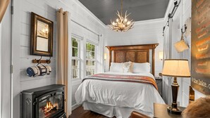 A cozy bedroom with a large bed, a fireplace, and a chandelier. - Stylish Creekside Escape | Pool + Hot Tub (Blue Eye)