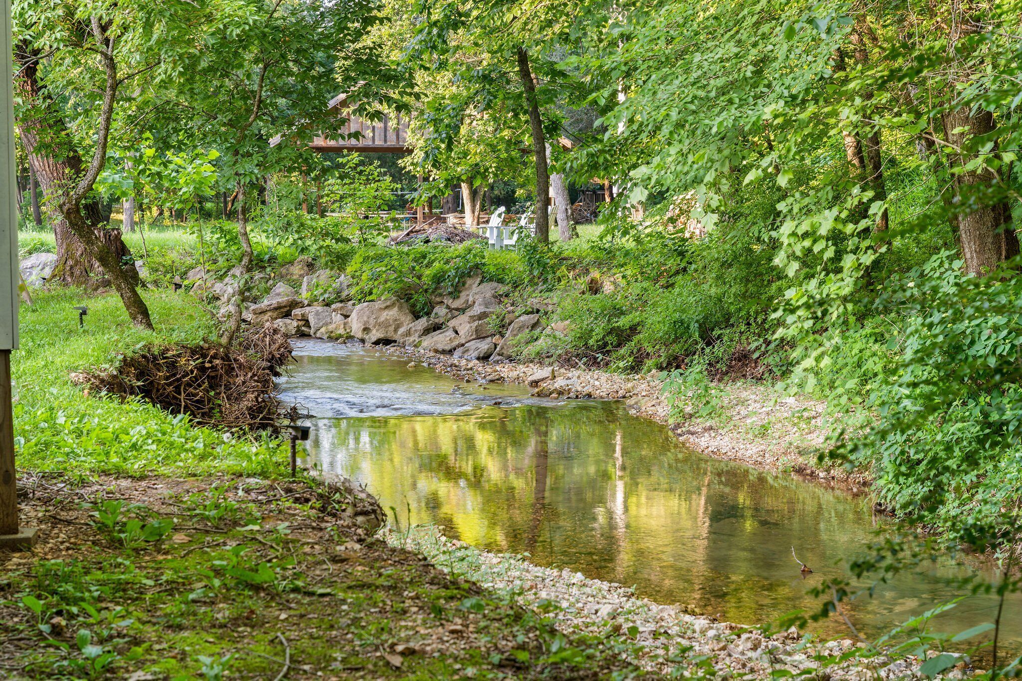 A serene outdoor setting with a small stream, lush greenery, and a rustic stone wall.