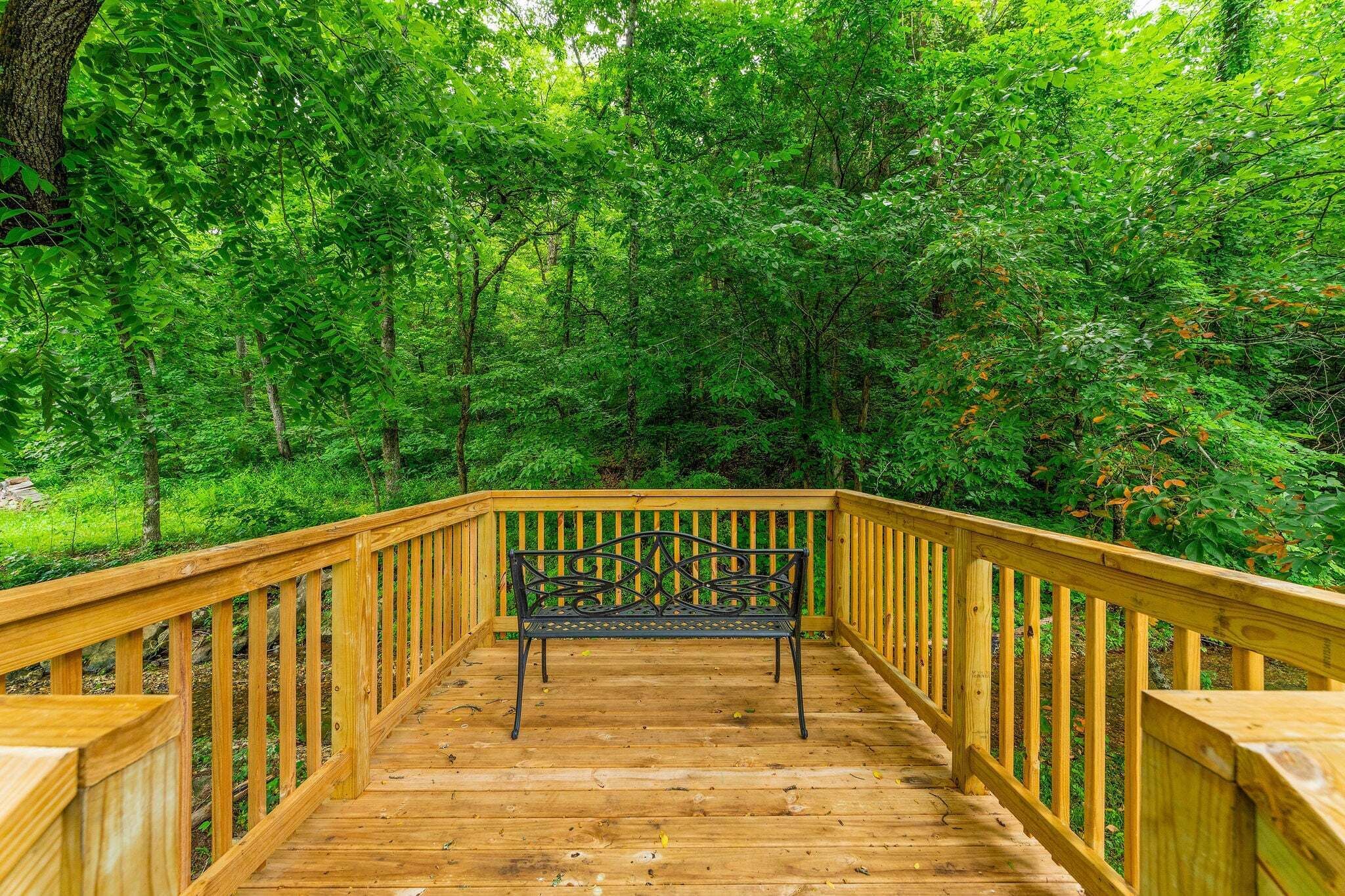 Eine Holzterrasse mit einer Bank, umgeben von dichtem Grün.