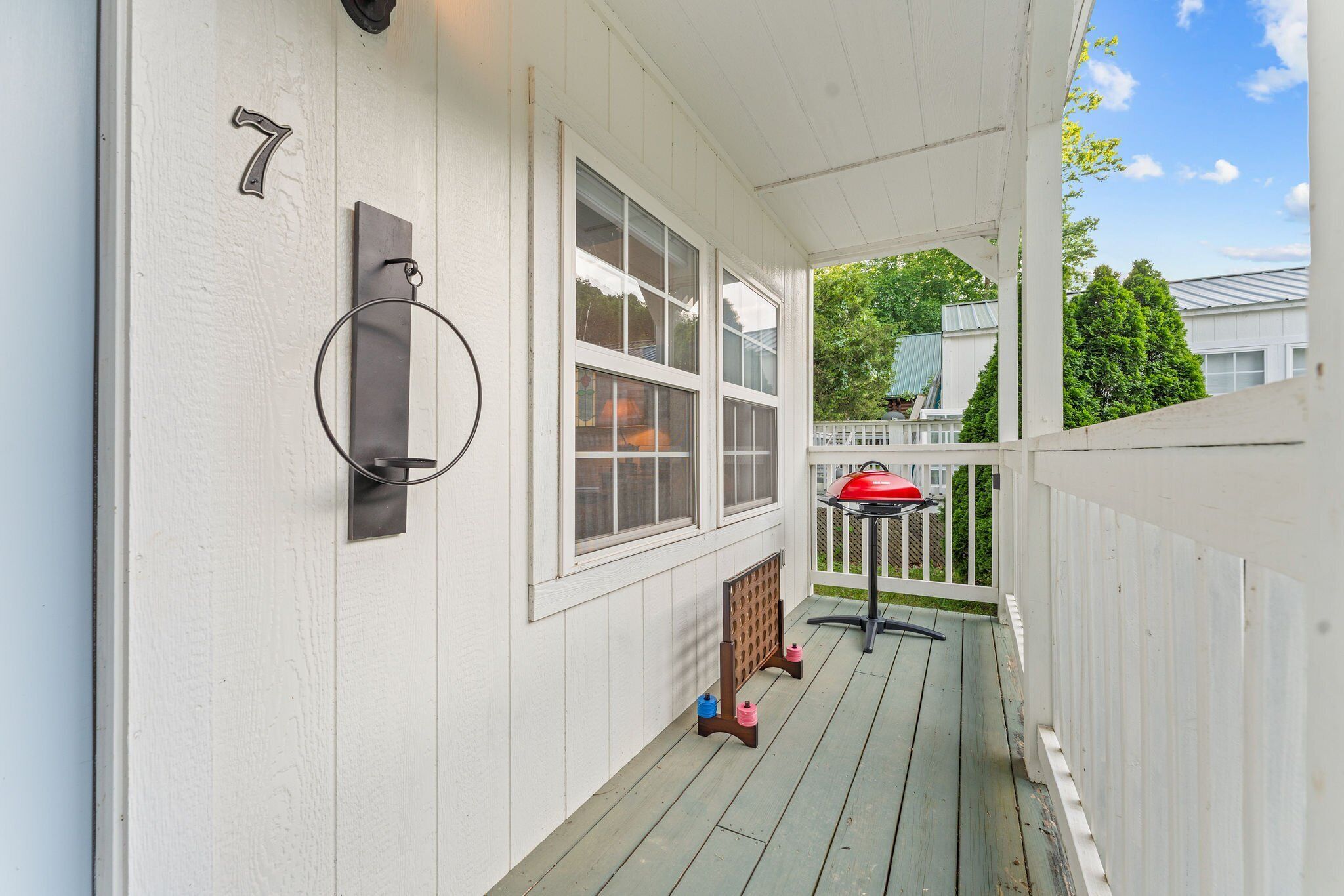 A porch with a white fence, a number 7 sign, a metal doorbell, and a red grill.