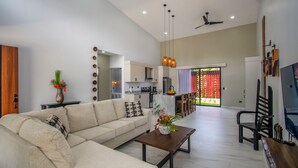A spacious living room with a large sofa, a coffee table, and a TV. There is a kitchen in the background with modern appliances and a dining area with chairs. - Charming Villa, 5 min walk to Marino Ballena Beach (Uvita)