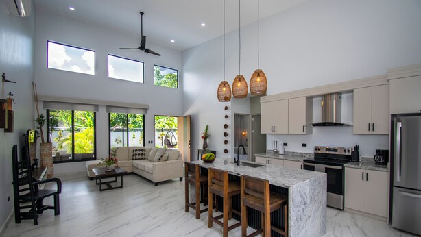 A spacious kitchen with a marble island, modern appliances, and large windows offering views of greenery. - Charming Villa, 5 min walk to Marino Ballena Beach (Uvita)