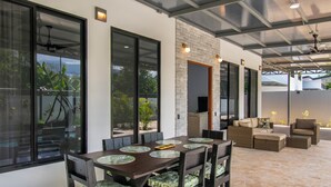A modern outdoor dining area with a brick wall, large windows, and a ceiling fan. - Charming Villa, 5 min walk to Marino Ballena Beach (Uvita)
