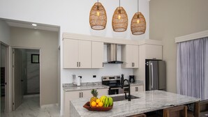 A modern kitchen with white cabinets, a granite countertop, a stainless steel refrigerator, and a fruit bowl on the island. - Charming Villa, 5 min walk to Marino Ballena Beach (Uvita)