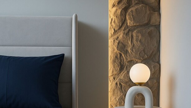 Een moderne slaapkamer met een bed, een nachtkastje met een lamp en een accentmuur van steen.