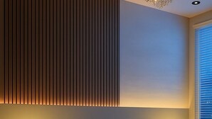 Een moderne slaapkamer met een bed, twee nachtkastjes met verlichte cijfers, een kroonluchter en een raam met jaloezieën.