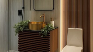 Een moderne badkamer met een vrijstaand toilet, een wastafel met gouden kom en een douchegedeelte.