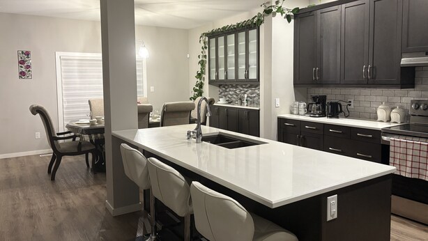A modern kitchen with dark cabinets, a white countertop, and a bar area with bar stools.