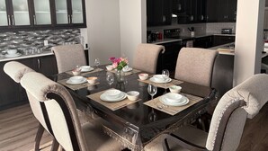A modern dining area with a dark wooden table, beige upholstered chairs, and a glass vase with pink flowers.