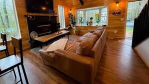 Un interior de cabaña acogedor, con chimenea, paredes de madera, un sofá y un televisor.
