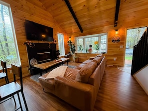 Ein gemütliches Blockhaus-Interieur mit Kamin, Holzwänden, einer Couch und einem Fernseher.