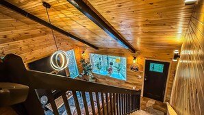 Interior de madera con una escalera que baja a un nivel inferior, techo de madera y televisor montado en la pared.