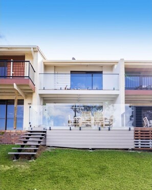 A modern two-story house with a balcony, outdoor seating, and a clear view of the sky.