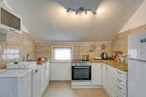 A kitchen with a built-in oven, a sink, a window with curtains, and a countertop with various items.