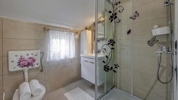 Un baño con inodoro, lavamanos, ducha con puertas de cristal y adhesivos decorativos de mariposas.
