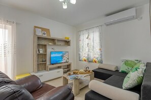 Ein Wohnzimmer mit Fernseher, Sofa, Couchtisch und Zierkissen.