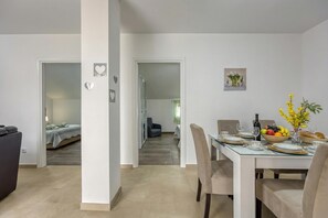 Een eethoek met een tafel voor vier personen, een bank en een bed op de achtergrond.