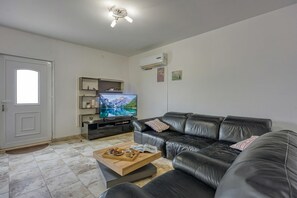 A living room with a black leather sofa, a wooden coffee table with a tray of pastries, a television on a stand, and a door with a white frame.