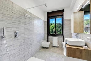 A modern bathroom with a shower, a toilet, a sink, and a window with a view of greenery.