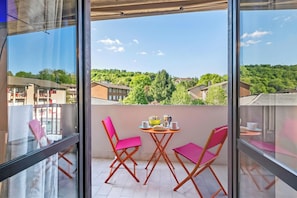 A balcony with a table and chairs, a view of buildings and greenery, and a clear sky.