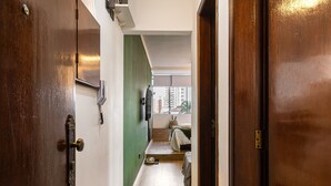 A hallway with wooden flooring, a green accent wall, and a bed with a view to a cityscape. - ARK Houses - Studio Completo no Gonzaga (Santos)