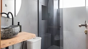 A modern bathroom with a stone sink, toilet, and glass shower enclosure. - ARK Houses - Studio Completo no Gonzaga (Santos)