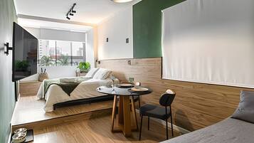 Una habitación de hotel moderna con cama, una mesita con sillas, televisor y vista a la ciudad.