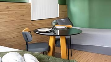 Una habitación moderna con paredes verdes, un panel de madera decorativo, una cama con ropa blanca, una mesa redonda con sillas y una lámpara colgante.