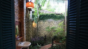 A narrow brick pathway leading to a rustic outdoor area with a brick sink and hanging light fixture. - Vamxang Rustic Home (Can Tho)