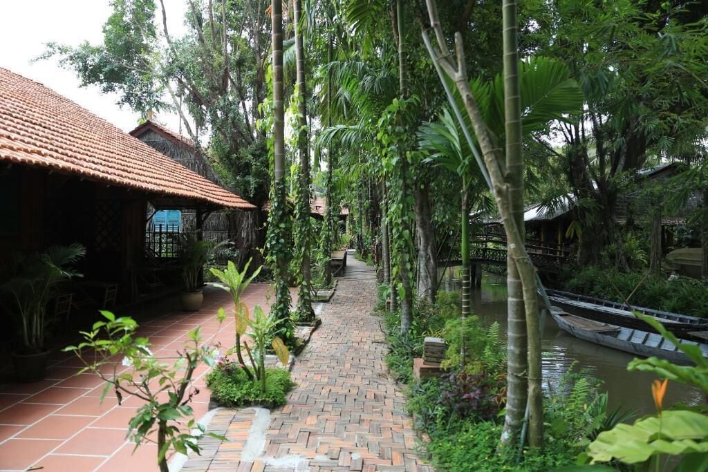 A pathway lined with lush greenery and a small boat on a waterway.