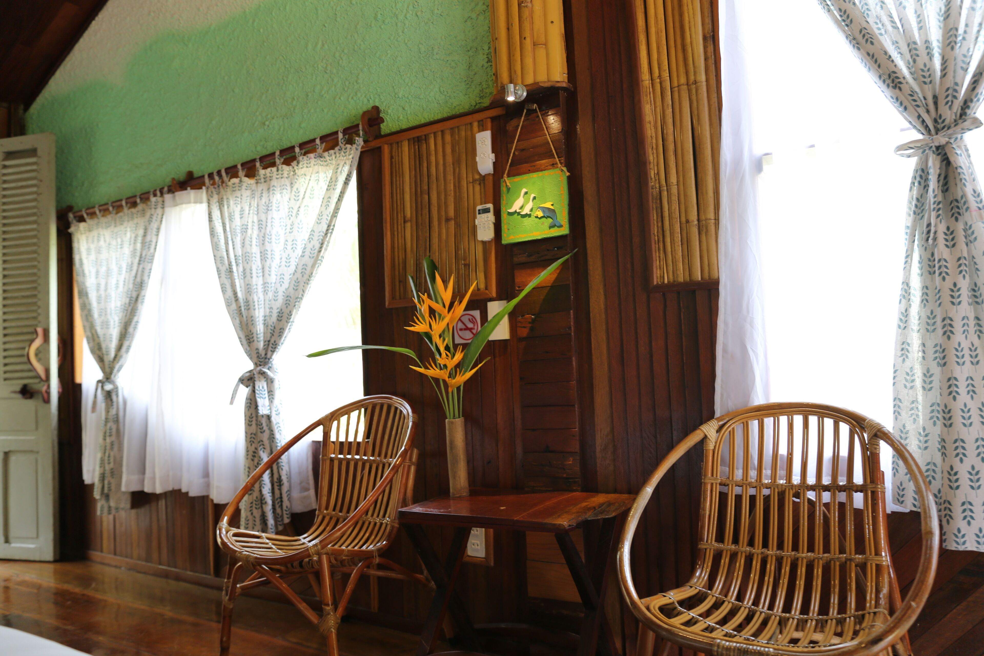 A room with wooden walls, two wicker chairs, a small table, and a vase with flowers.