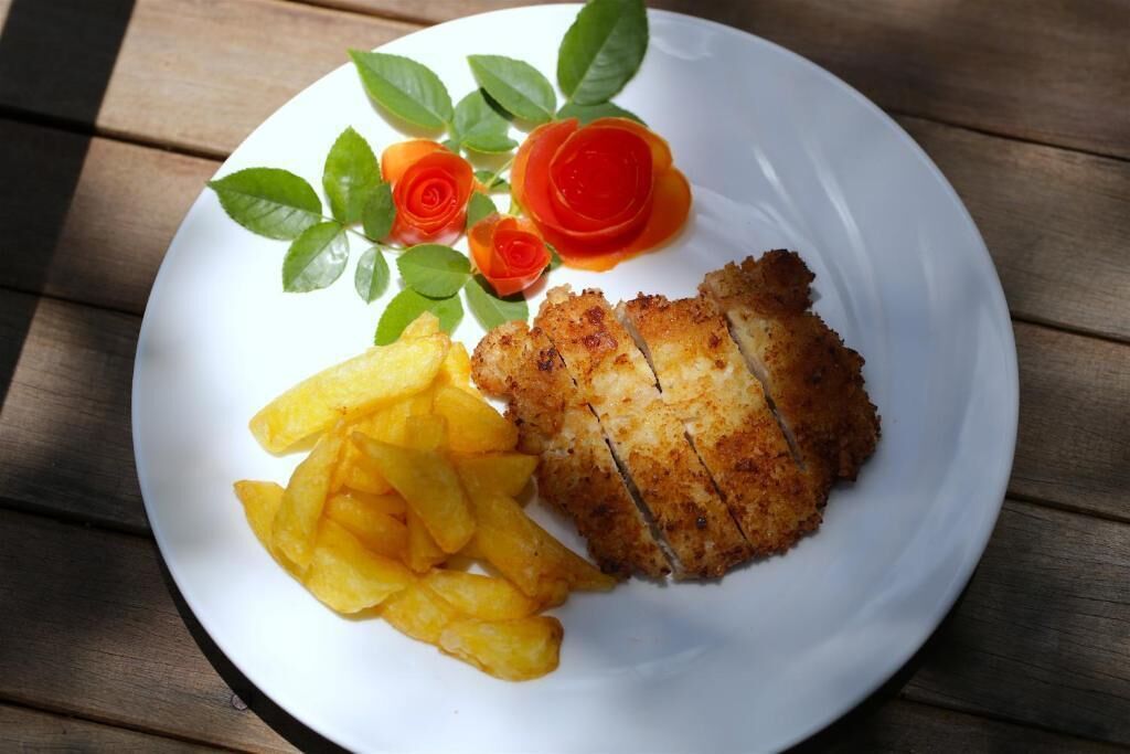Un plato con pescado empanizado, papas fritas y rodajas de tomate decorativas sobre una mesa de madera.