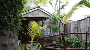 A rustic wooden house with a thatched roof, surrounded by lush greenery and a wooden bridge. - Vamxang Rustic Home (Can Tho)
