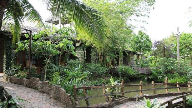 A garden with a brick pathway, a wooden bridge over a pond, and various tropical plants. - Vamxang Rustic Home (Can Tho)