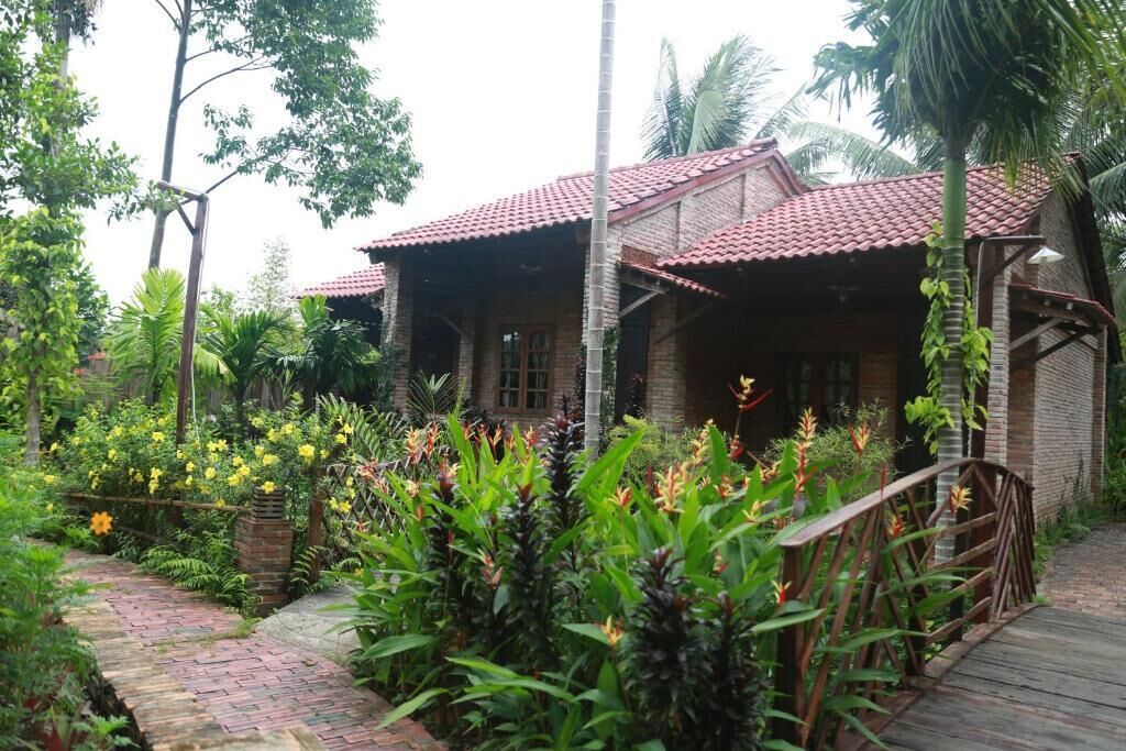 Une maison traditionnelle avec un toit en tuiles, entourée d’une végétation luxuriante et de plantes en fleurs.