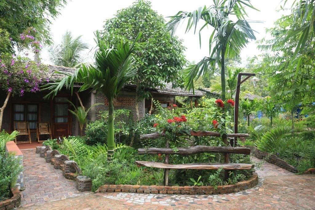 A rustic garden with a wooden bench, a brick pathway, and lush greenery.
