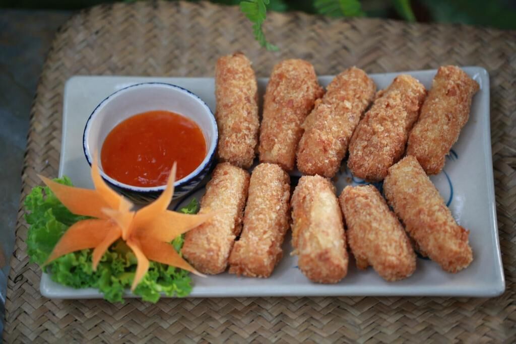 A plate of breaded and fried items, possibly chicken tenders, served with a side of red sauce and garnished with a carrot flower on lettuce.