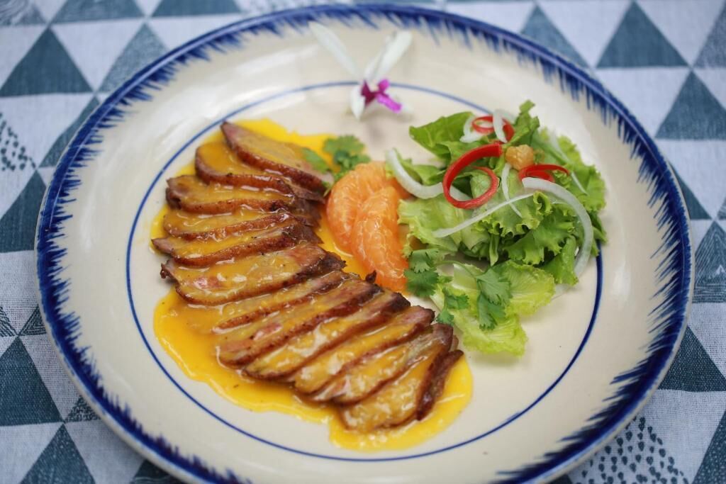 A plate with sliced meat, vegetables, and a small flower.