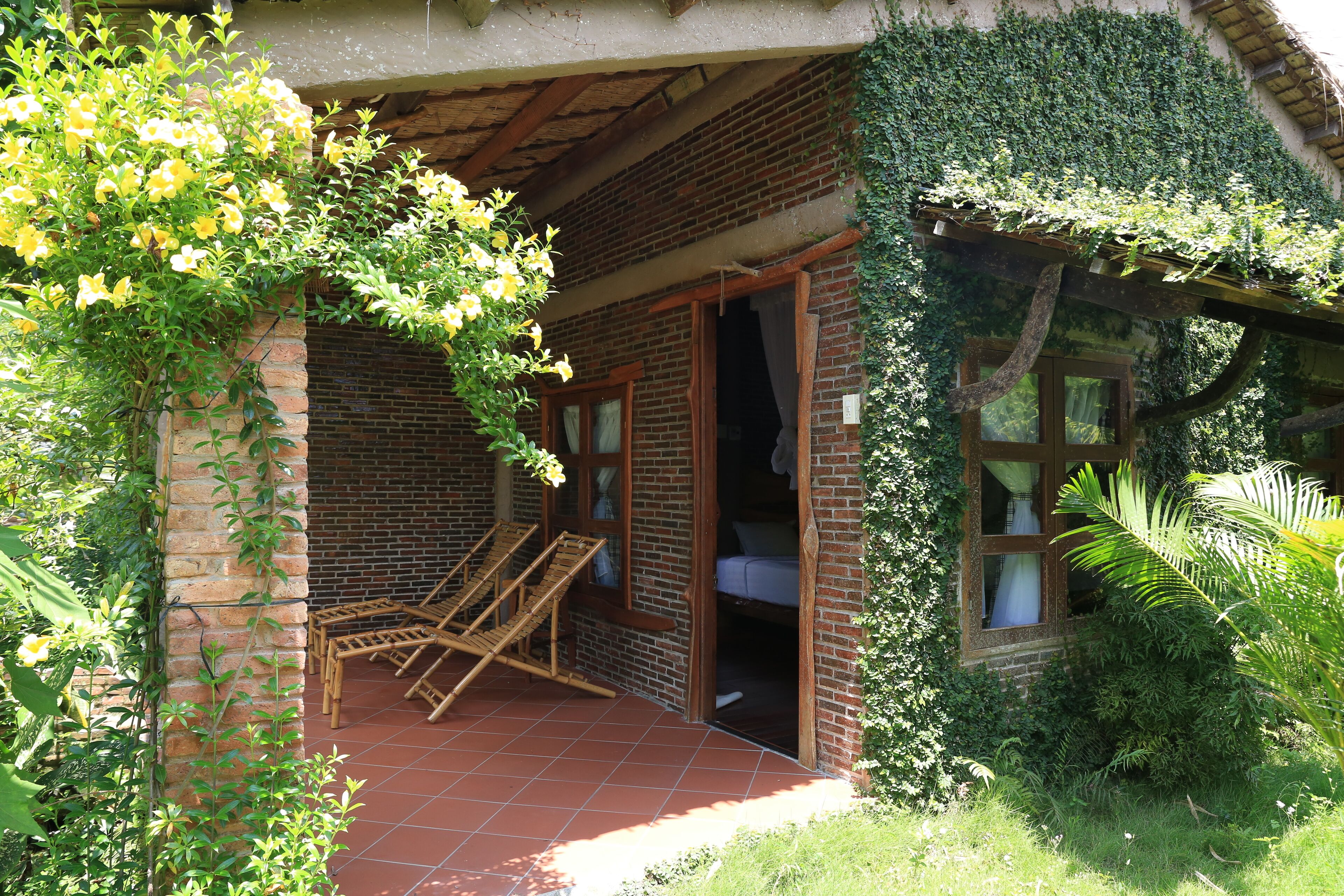 Un bâtiment rustique avec une façade en briques, une porte en bois et un petit porche agrémenté de deux chaises en bois.