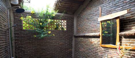 A rustic bathroom with a brick wall, a wooden-framed mirror, a white sink, and a shower area.