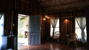 A wooden interior with a dining area, wicker chairs, a table with a bowl of fruit, and a door leading outside. - Vamxang Rustic Home (Can Tho)