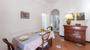 Ein Essbereich mit einem für zwei Personen gedeckten Tisch, Stühlen, einem Schrank mit einer Lampe und einem gerahmten Bild an der Wand.