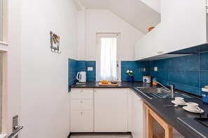 A compact kitchen with white cabinets, a black countertop, and blue tiles.