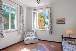 A room with a chair near a window, a bed with a lamp, and a framed picture on the wall. - Middle Apartment Vernazza, Vernazza, Italy (Vernazza)