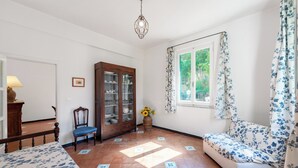 Ein Zimmer mit Holzschrank, Stuhl, Sofa, Fenster mit Vorhängen und einer Pendelleuchte.