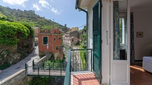 Un balcon donnant sur un village perché sur une colline, une porte blanche et un lit dans la chambre.